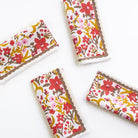 A set of four folded cloth napkins with a floral pattern in red, yellow, and brown colors on a white background, displayed against a neutral background.