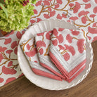 A set of folded cotton napkins with a ginkgo leaf pattern in coral hues, displayed on a stack of white plates.