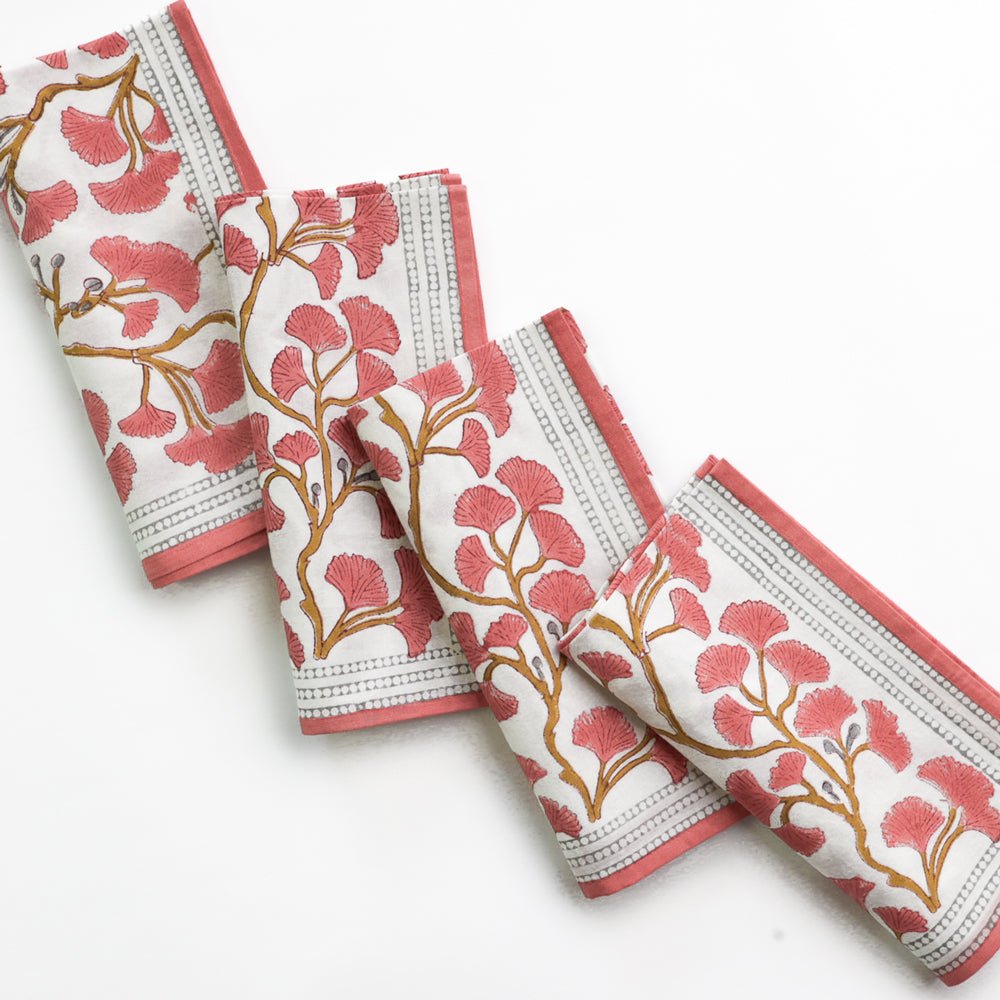 A set of folded cotton napkins with a ginkgo leaf pattern in coral hues