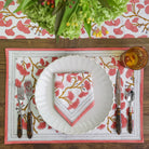 A coral and white placemat with a ginkgo leaf design, displayed on a table with dinnerware.