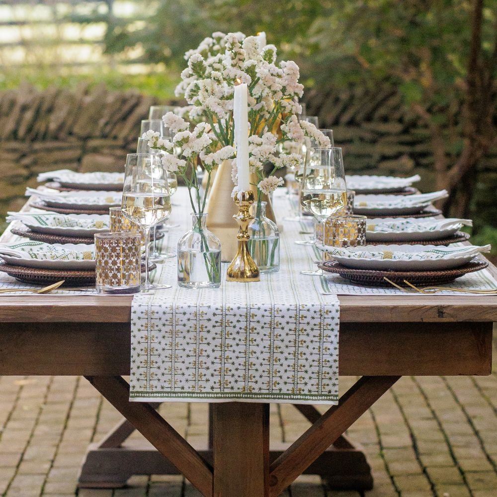 A hunter green table runner with a palm tree pattern displayed on a table set for dining.