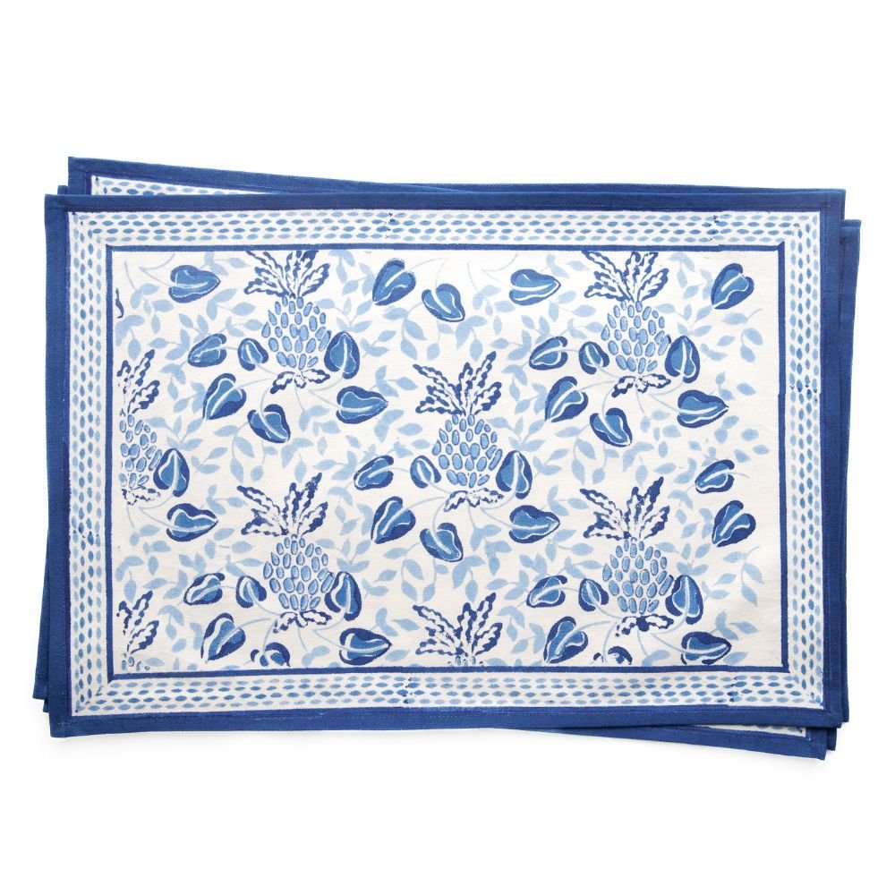 A set of blue and white placemats with a floral and pineapple pattern.