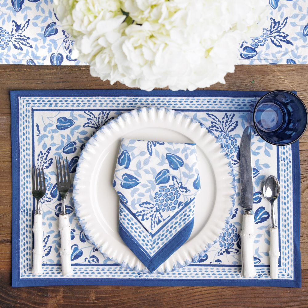 Blue and white floral table setting with plates, cutlery, and napkins on a wooden table.
