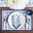 Blue and white floral table setting with plates, cutlery, and napkins on a wooden table.