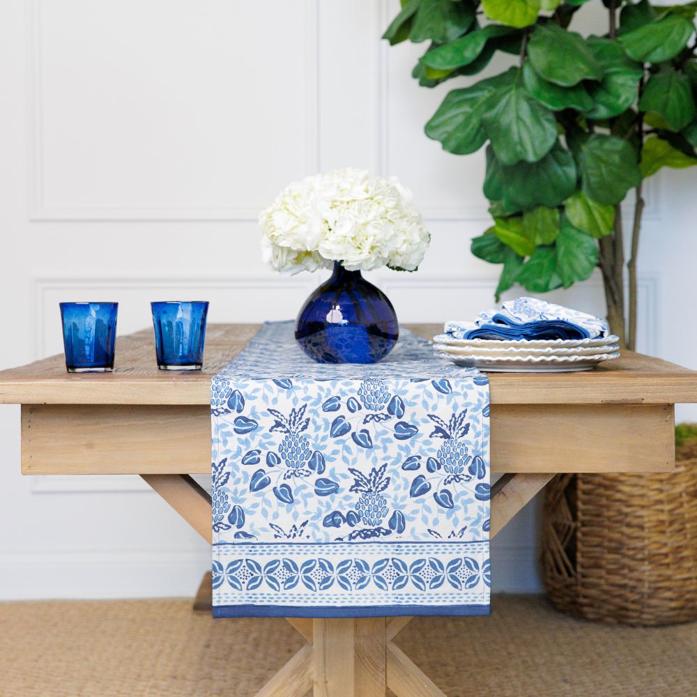 A blue and white table runner with a pineapple pattern displayed on a wooden table.