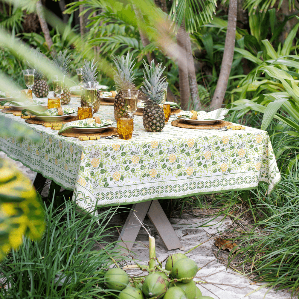 Table set for a meal outdoors with a floral tablecloth, pineapple decorations, and tropical plants.