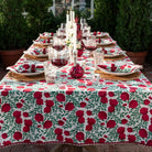 A tablecloth with a red pomegranate and green leaf pattern laid out on a table set for a meal, featuring dishes and glasses.