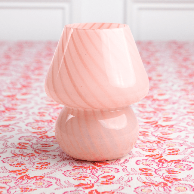 A pink lamp with a conical shade placed on a patterned surface.