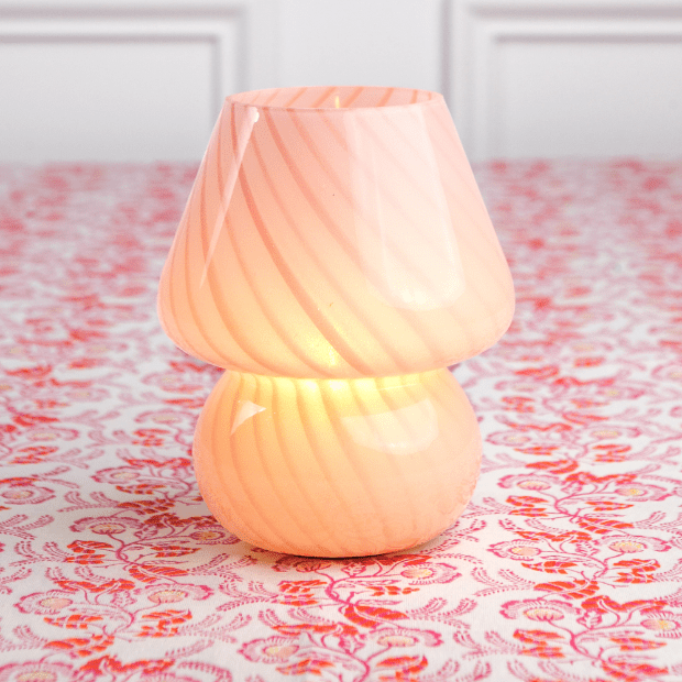 A pink lamp with a conical shade placed on a patterned surface.