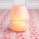A pink lamp with a conical shade placed on a patterned surface.