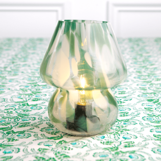 A green lamp with a conical shape on a green patterned tablecloth