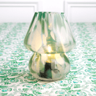 A green lamp with a conical shape on a green patterned tablecloth