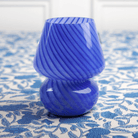 A vibrant blue lamp with a swirling pattern, resembling a vase shape, placed on a table with a floral pattern.