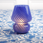 A cobalt blue lamp with a conical shape on a blue patterned tablecloth