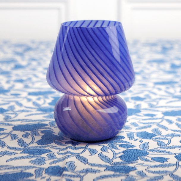 A cobalt blue lamp with a conical shape on a blue patterned tablecloth