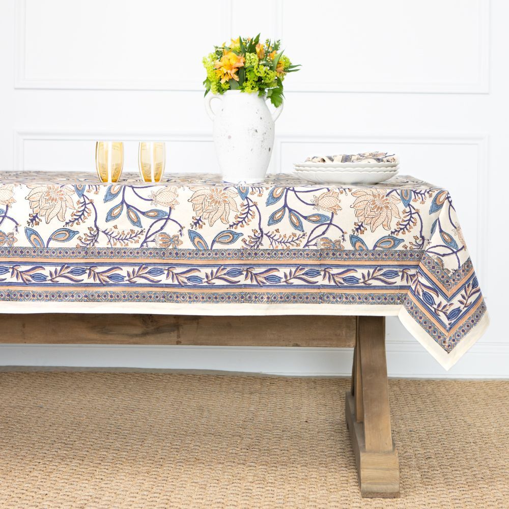 Tablecloth with floral pattern on a wooden table against a white wall.