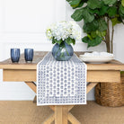 Table setting with a blue and white patterned table runner, flowers, and bowls on a wooden table.