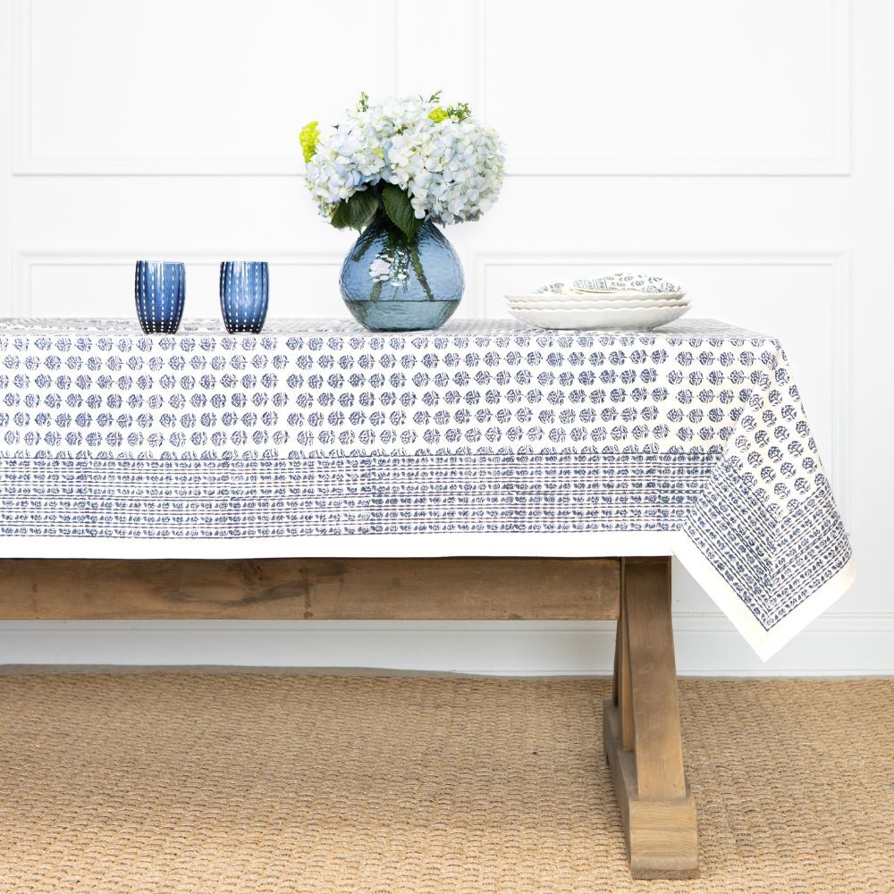 Tablecloth with floral pattern on a wooden table against a white wall.