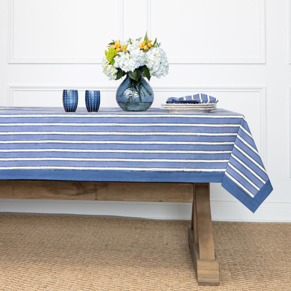 Table with a blue and white striped tablecloth, flowers, and glasses on a wooden floor.