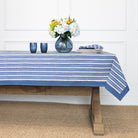 Table with a blue and white striped tablecloth, flowers, and glasses on a wooden floor.