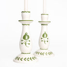 Pair of white candlesticks with green floral patterns on a white background