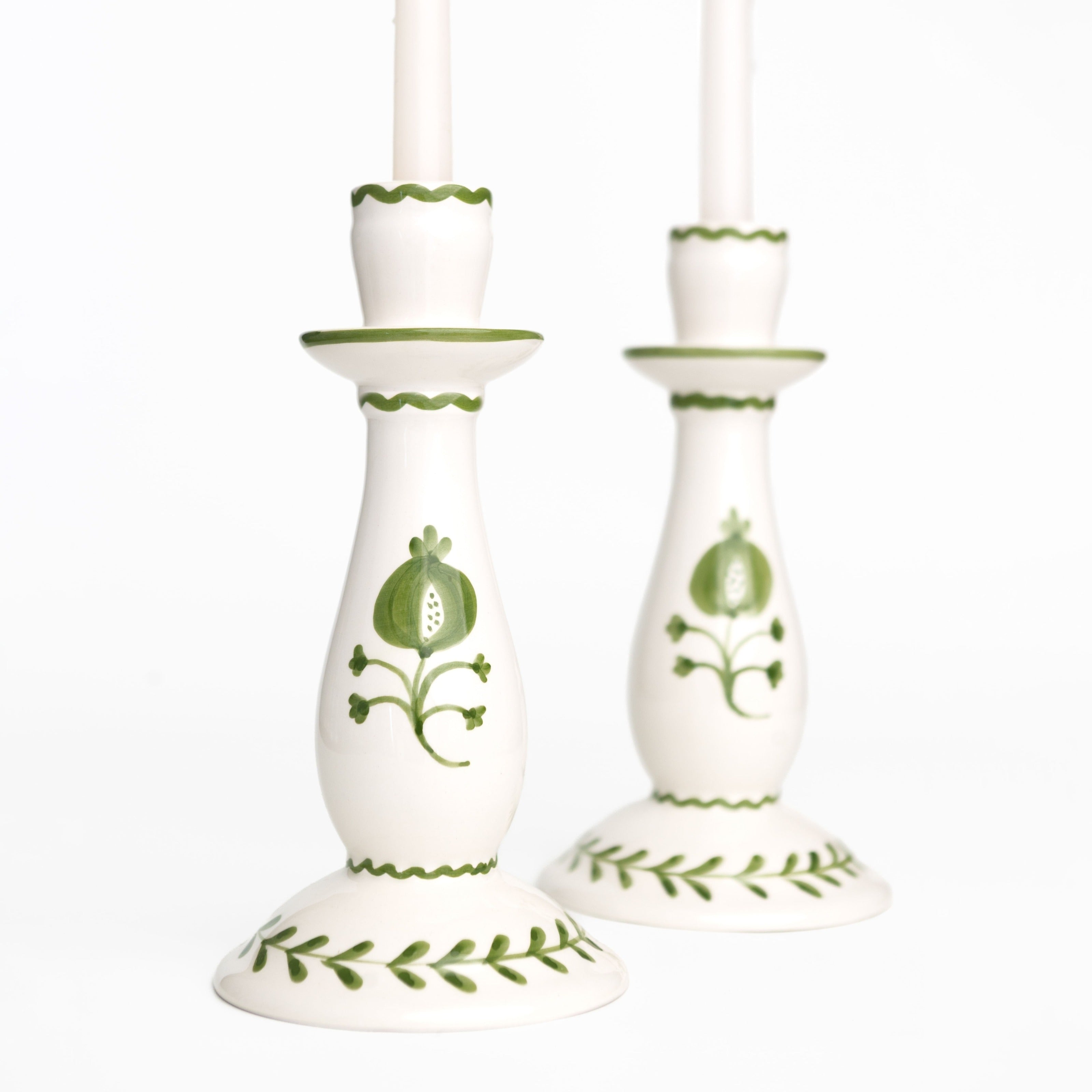 Pair of white candlesticks with green floral patterns on a white background