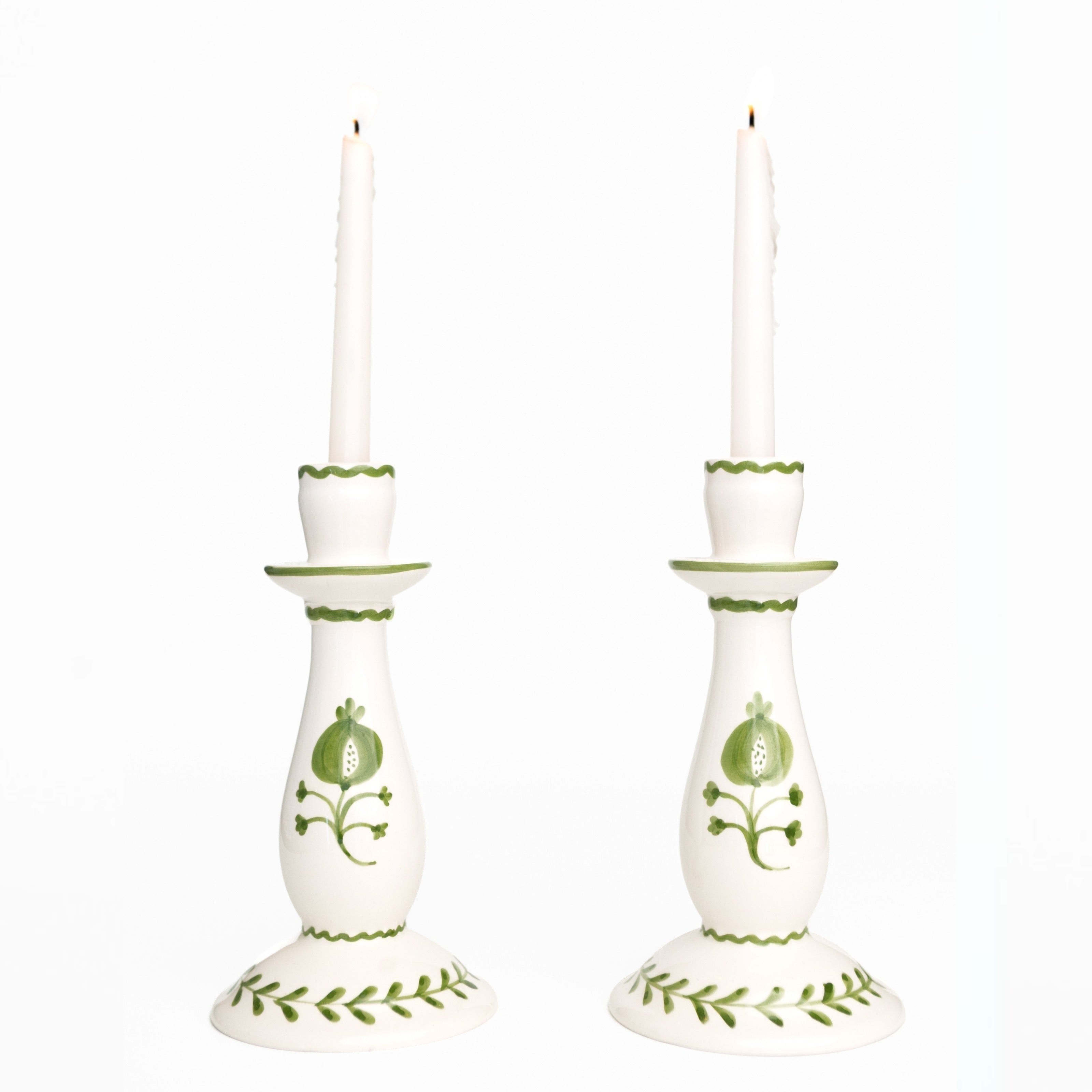 Pair of white candlesticks with green decorative patterns on a white background