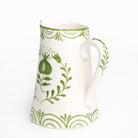 White ceramic pitcher with green leaf and pomegranate pattern on a white background