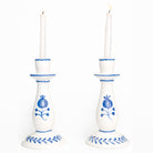 White candle holders with cobalt blue floral designs and white candles on a white background