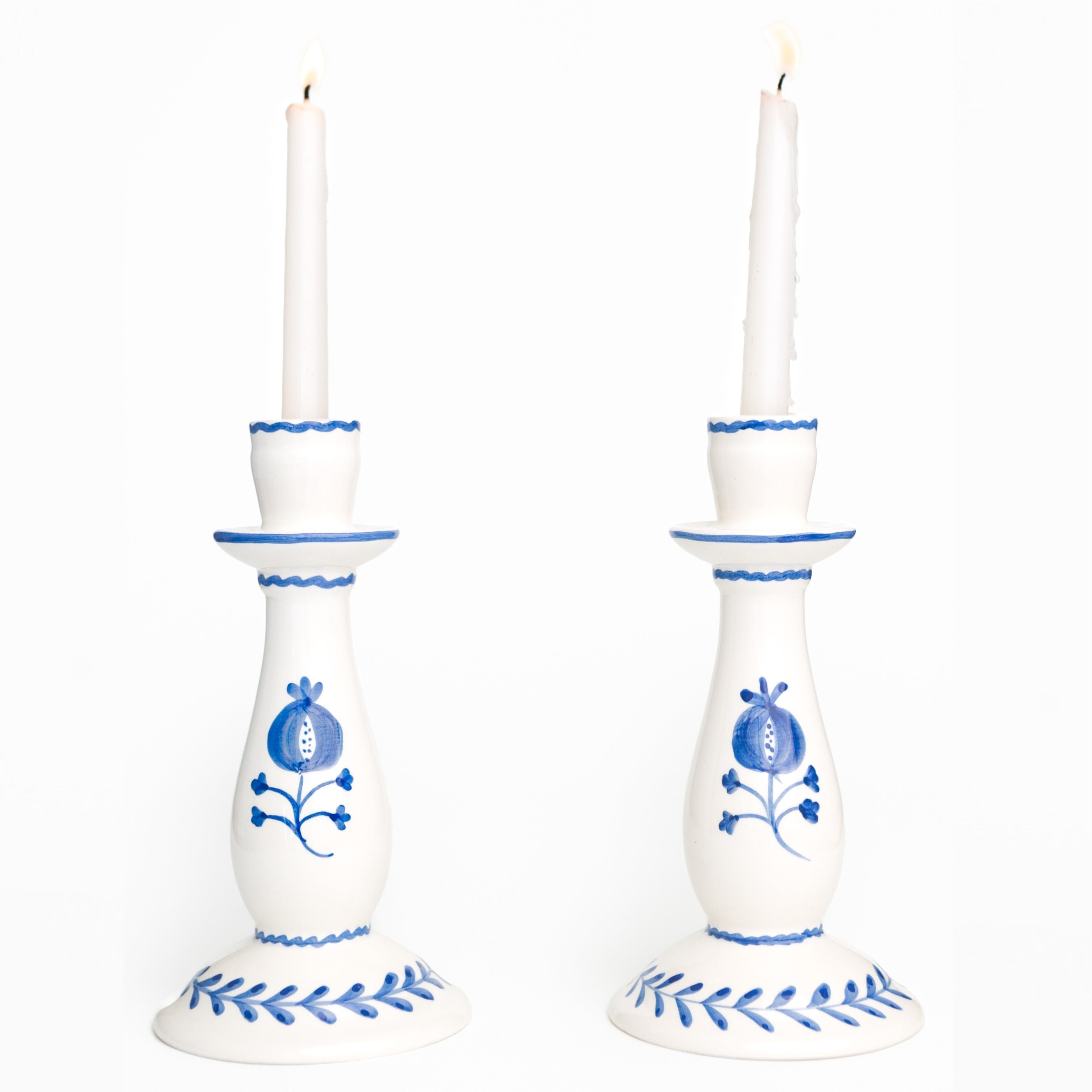 White candle holders with cobalt blue floral designs and white candles on a white background