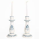 Two white candlesticks with blue floral designs holding candles on a white background
