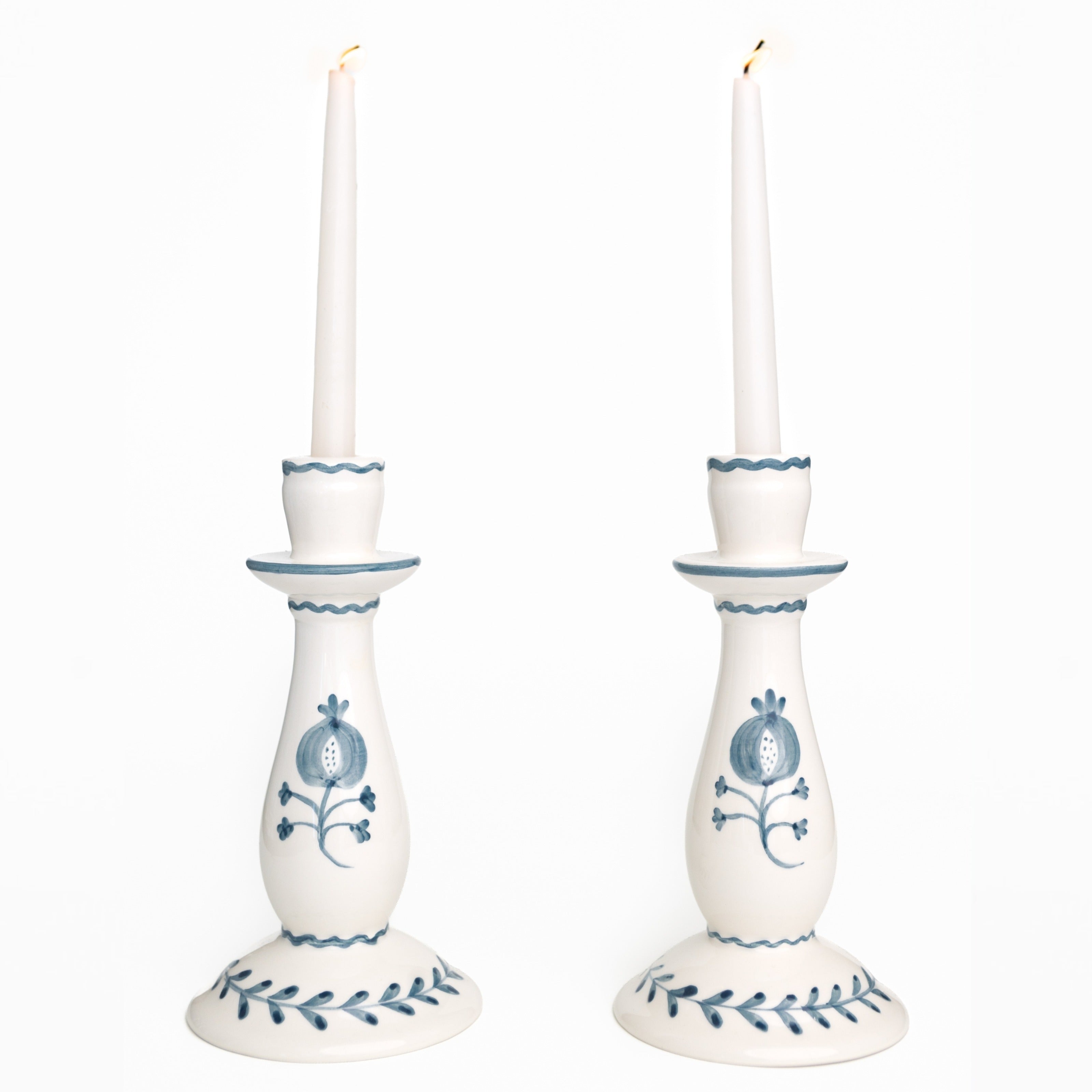 Two white candlesticks with blue floral designs holding candles on a white background