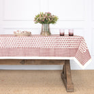 Tablecloth with a red floral pattern on a wooden table against a white wall.