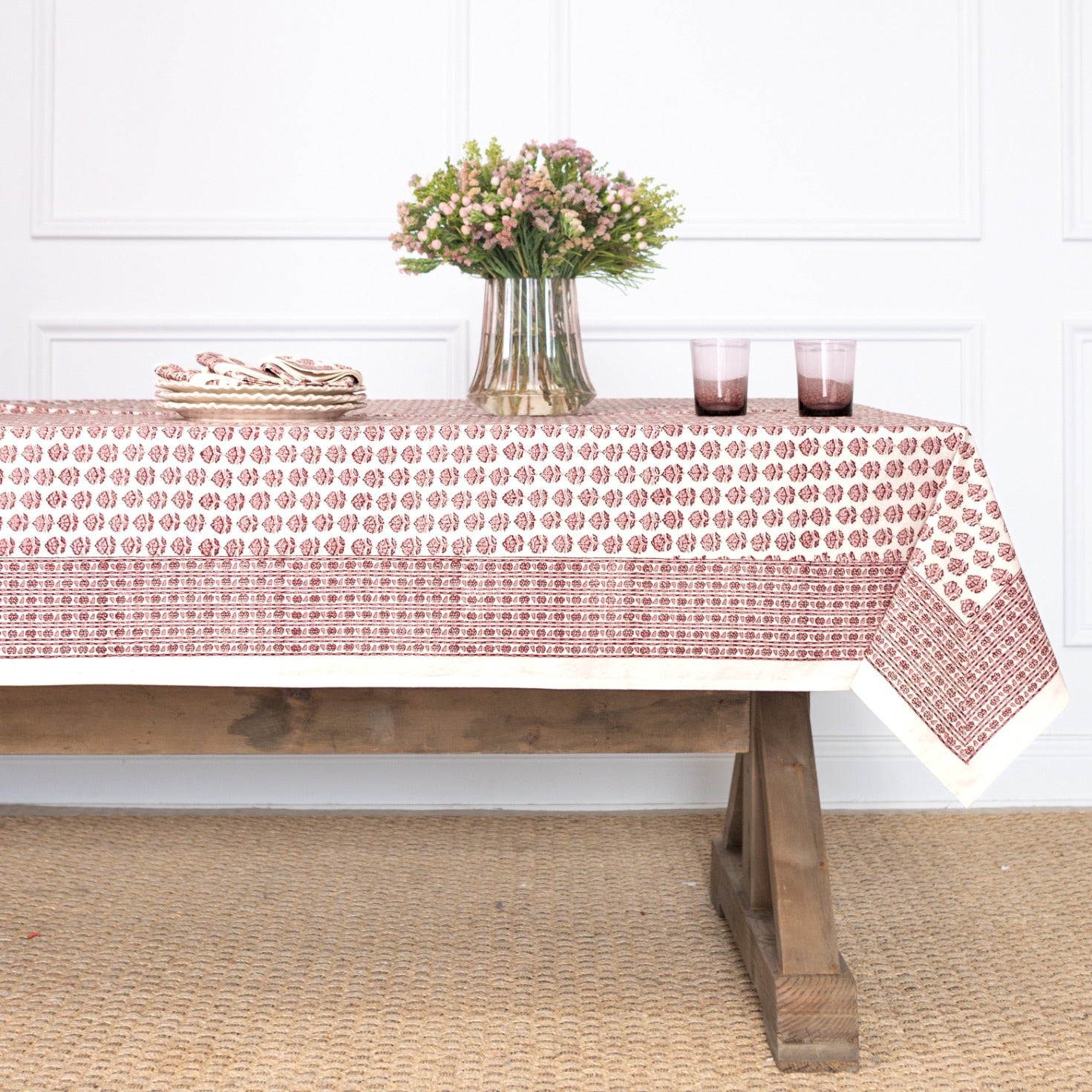 Tablecloth with a red floral pattern on a wooden table against a white wall.