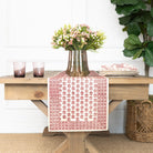 Dining table with a red and white patterned table runner, vase of flowers, and glasses.