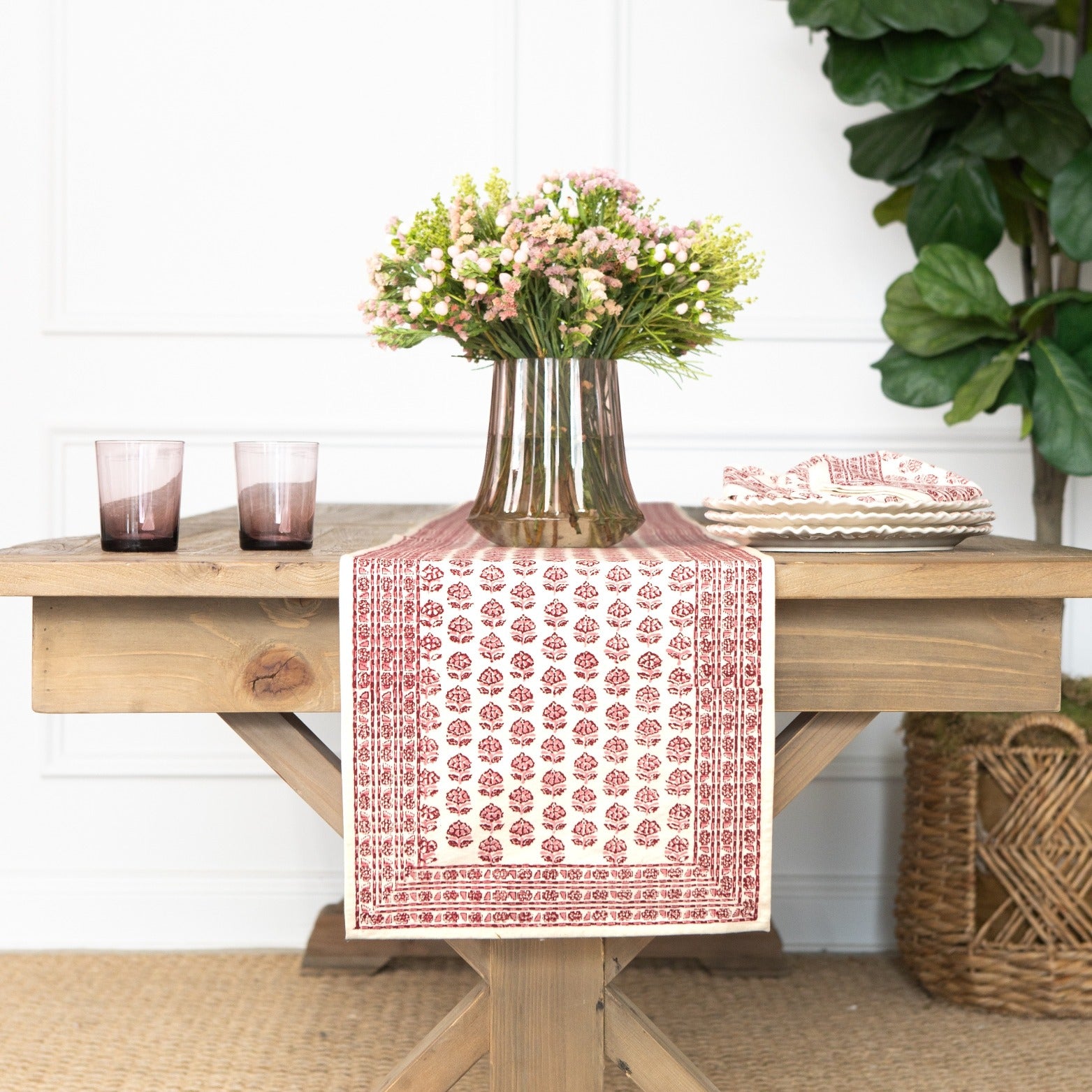 Dining table with a red and white patterned table runner, vase of flowers, and glasses.
