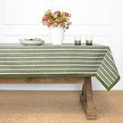 Green and white striped tablecloth on a wooden table with a vase of flowers and glasses.