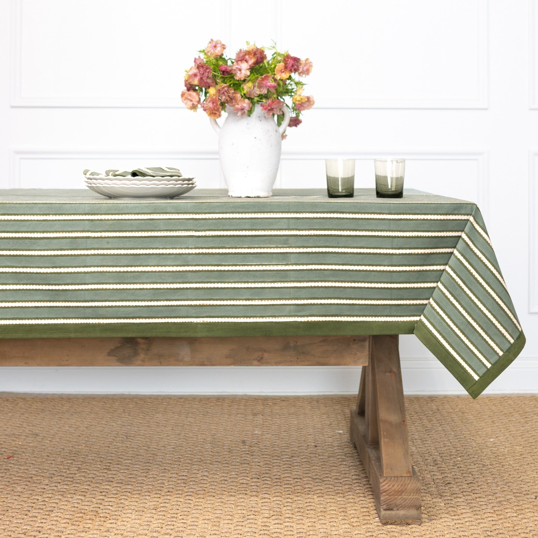 Green and white striped tablecloth on a wooden table with a vase of flowers and glasses.