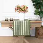 Green and white striped table runner on a wooden table with a vase of flowers and candles.