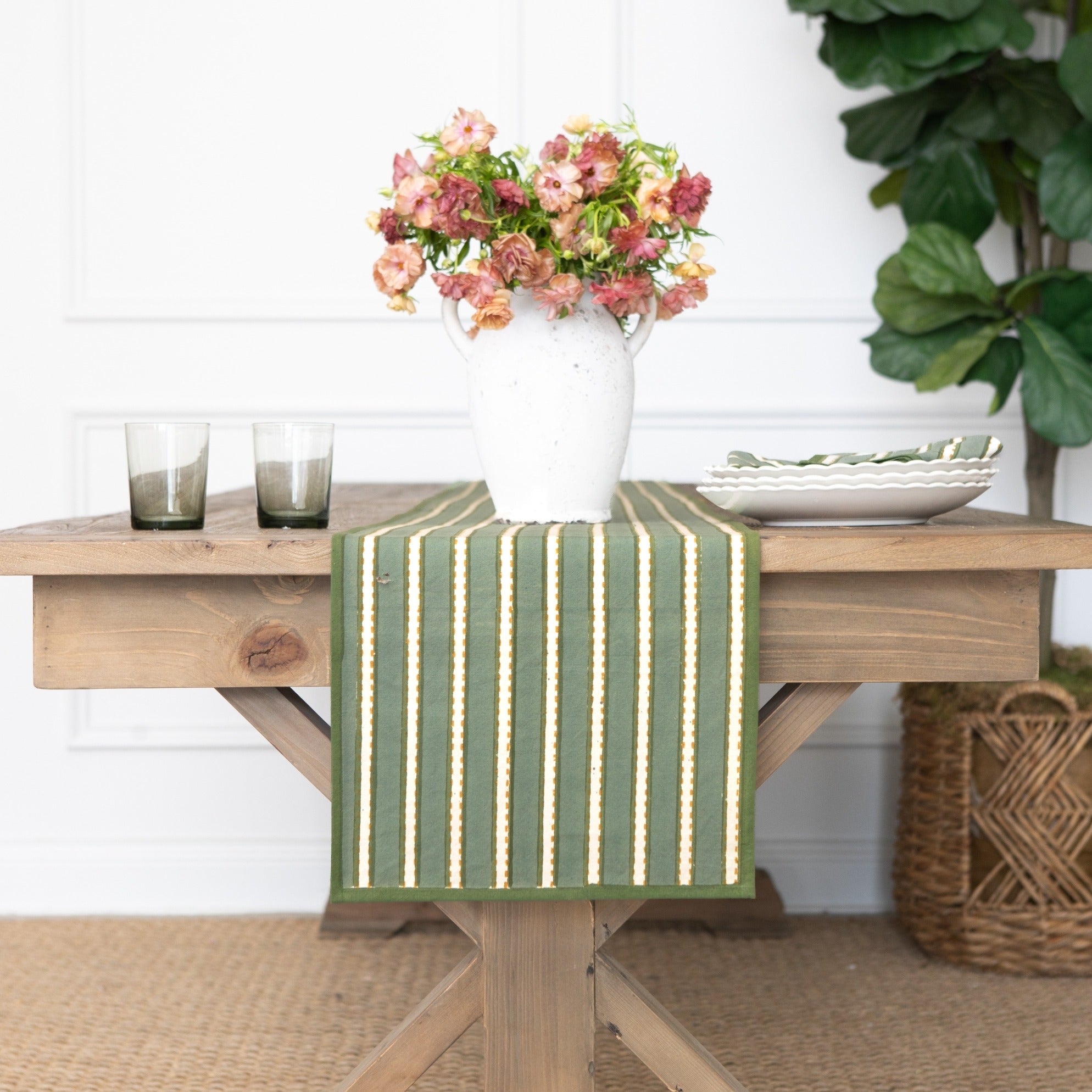 Green and white striped table runner on a wooden table with a vase of flowers and candles.