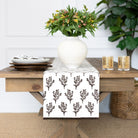 Table with a floral-patterned table runner, white vase with flowers, and glasses on a wooden table.