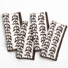 Set of four white napkins with brown leaf pattern on a white background