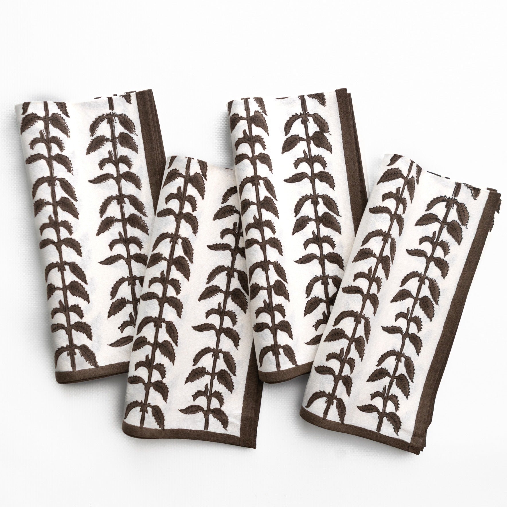 Set of four white napkins with brown leaf pattern on a white background