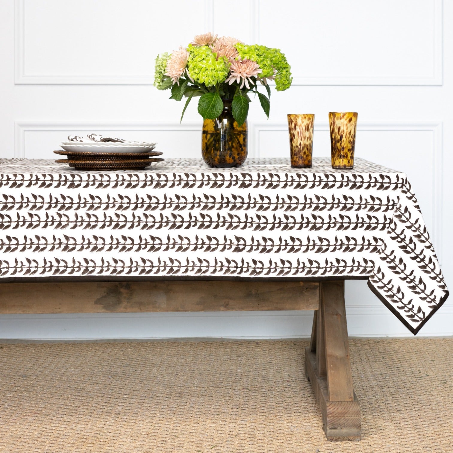 Tablecloth with decorative pattern on a wooden table with flowers and candles.