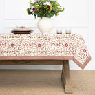 Table with floral tablecloth, vase of flowers, and glasses on a white wall background