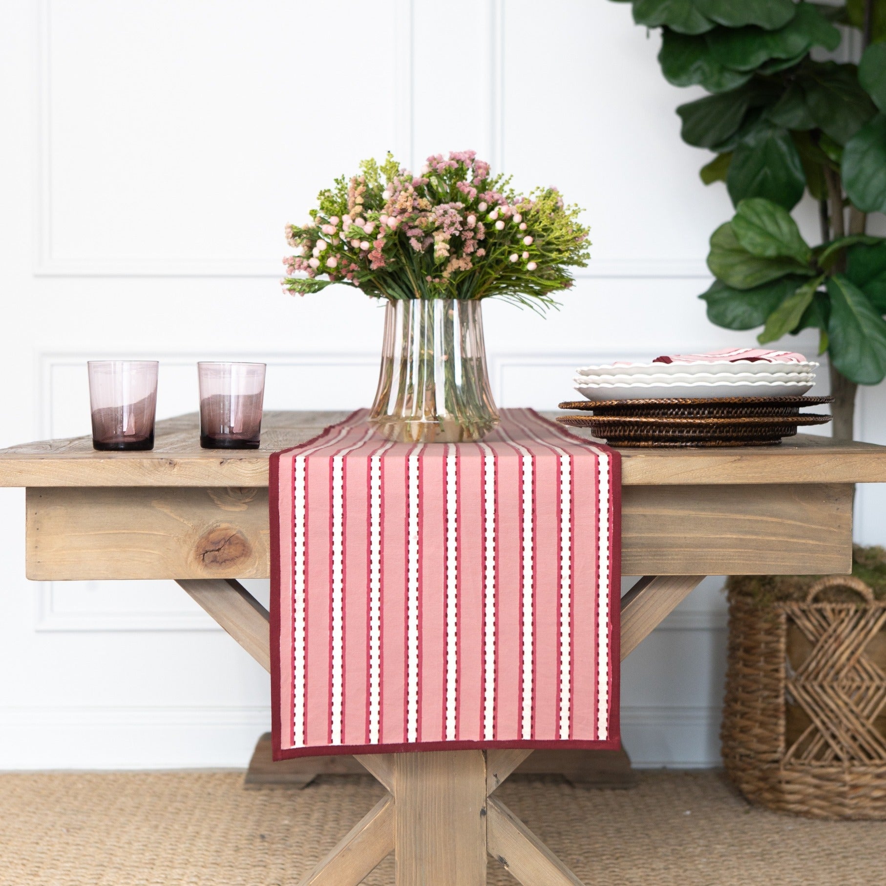 Table setting with a red and white striped table runner, flowers, and glasses on a wooden table.