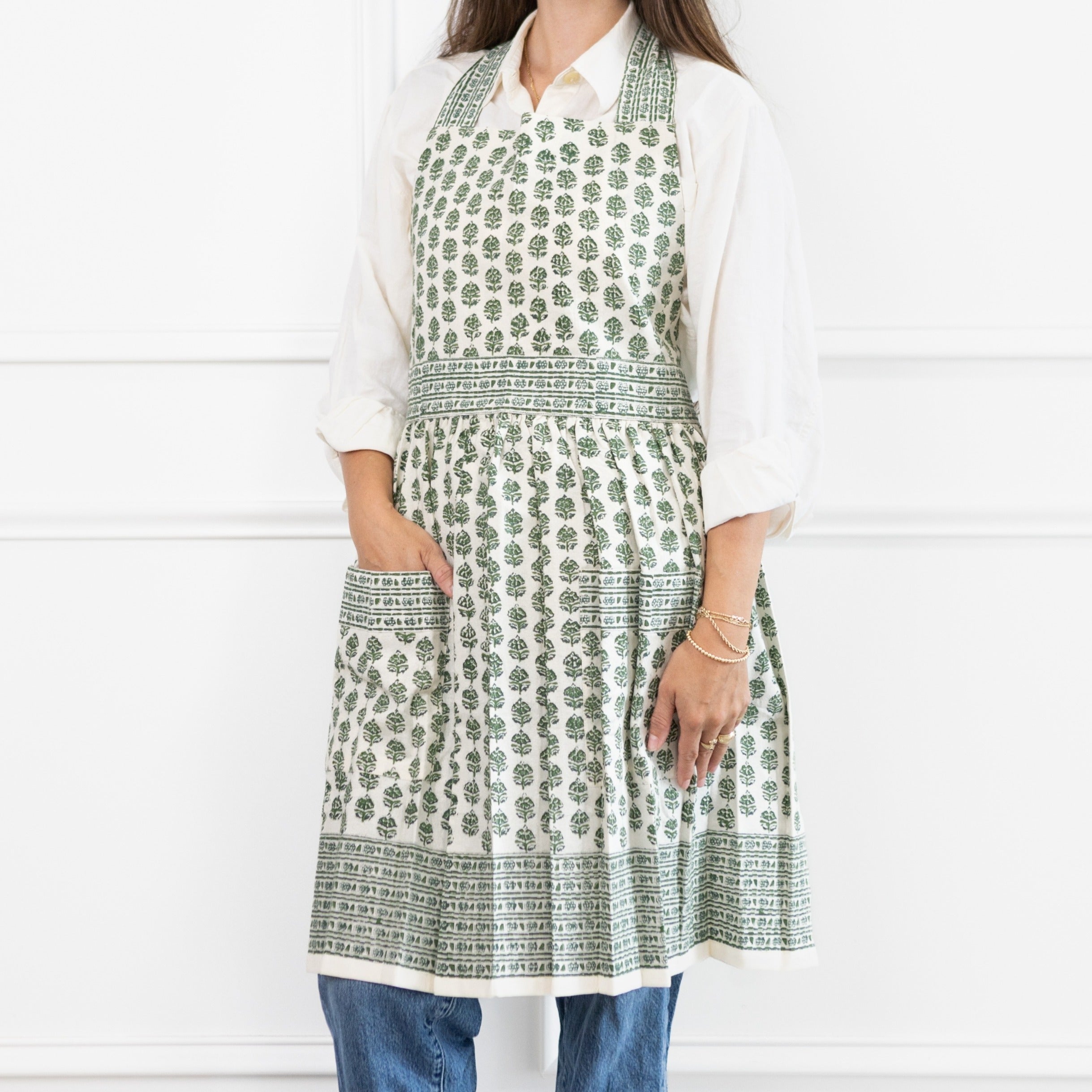 Person wearing a green and white patterned apron over a white shirt and blue jeans on a white background