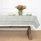 Table with a patterned tablecloth, flowers, and glasses in a room.
