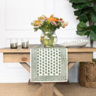 Table with a green patterned table runner, flowers, and candles on a wooden table.