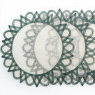 A set of round placemats with a central sun motif, predominantly white with green fretwork borders.